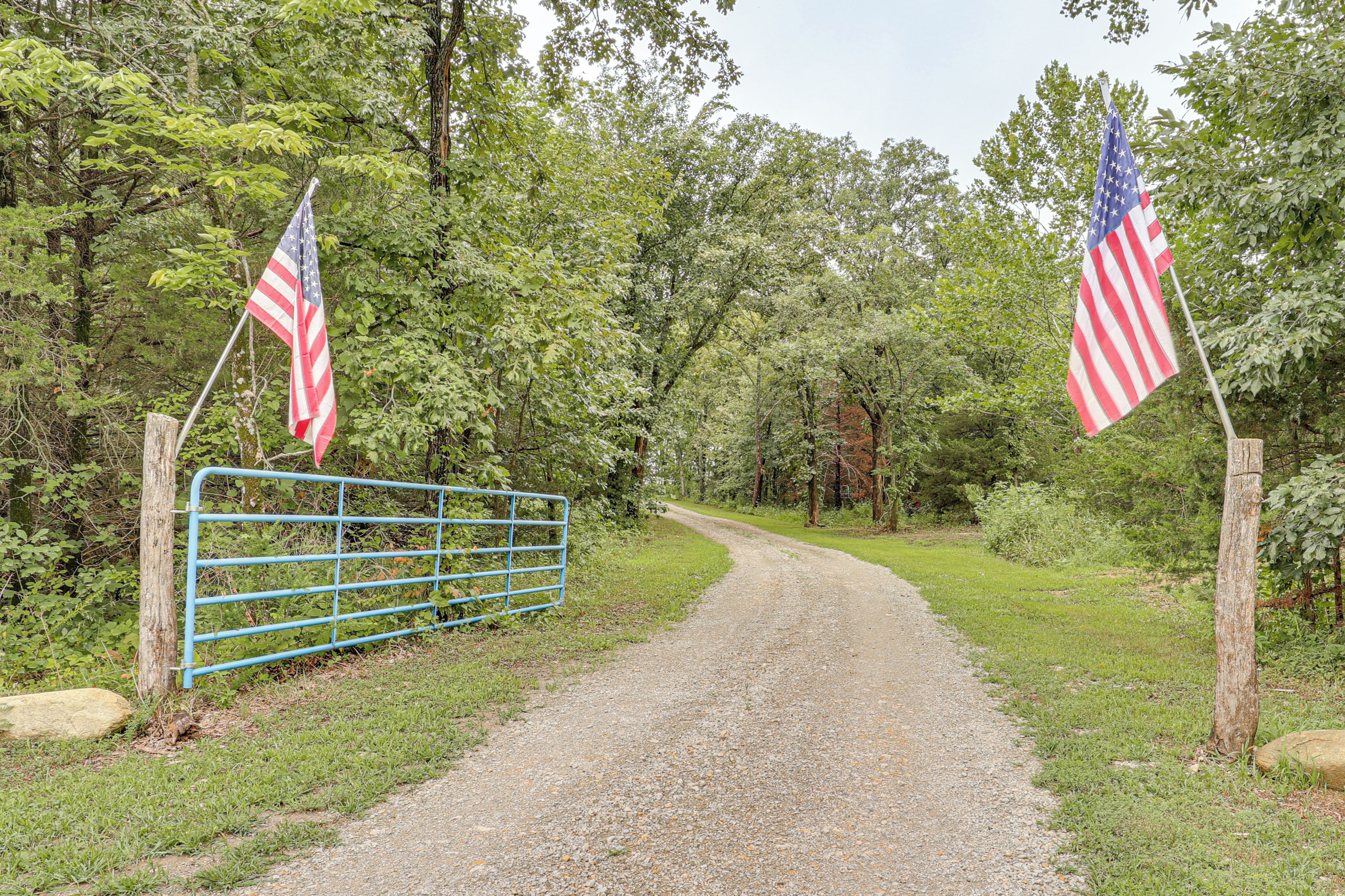 A gravel path leading through a wooded area with two American flags on flagpoles on either side.