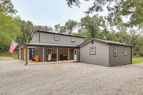 A two-story house with a covered porch, a barbecue grill, and an American flag.