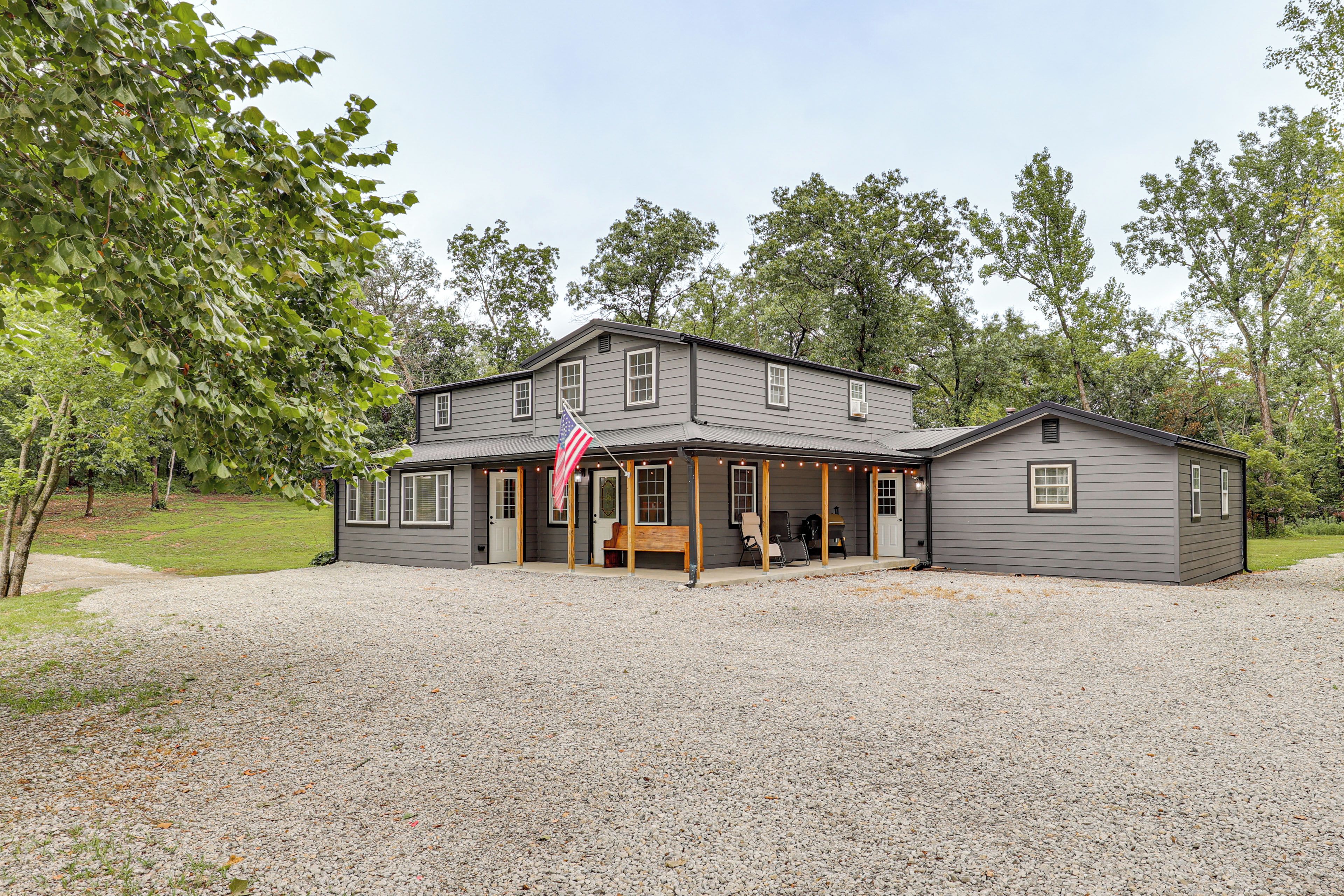 A two-story house with a porch, a flag, and a gravel driveway.