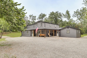A two-story house with a porch, a flag, and a gravel driveway.