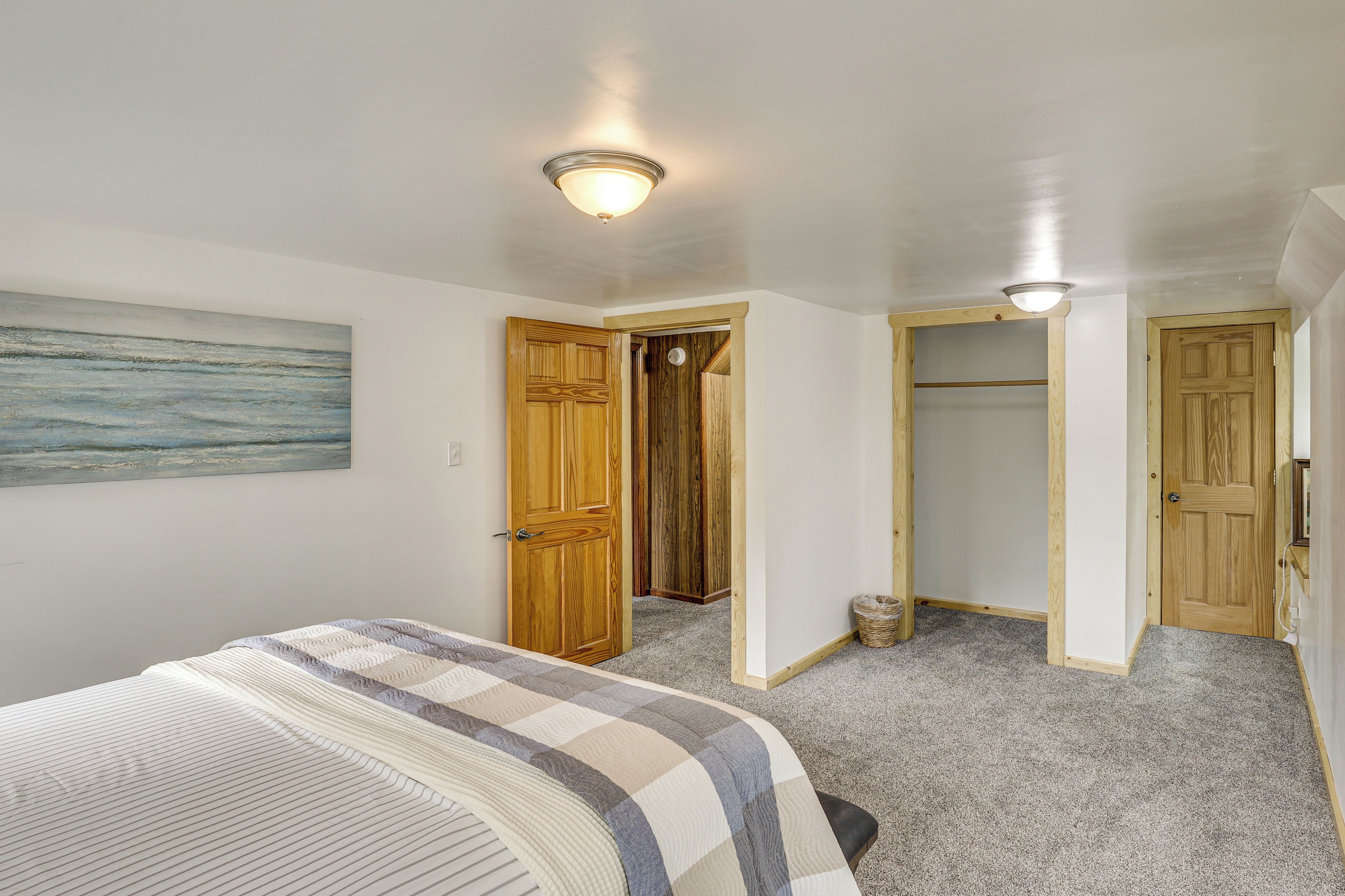 A bedroom with a bed, a wooden door, a closet, and a hallway leading to another room.