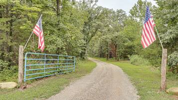 A gravel path leading through a wooded area with two American flags on flagpoles on either side.