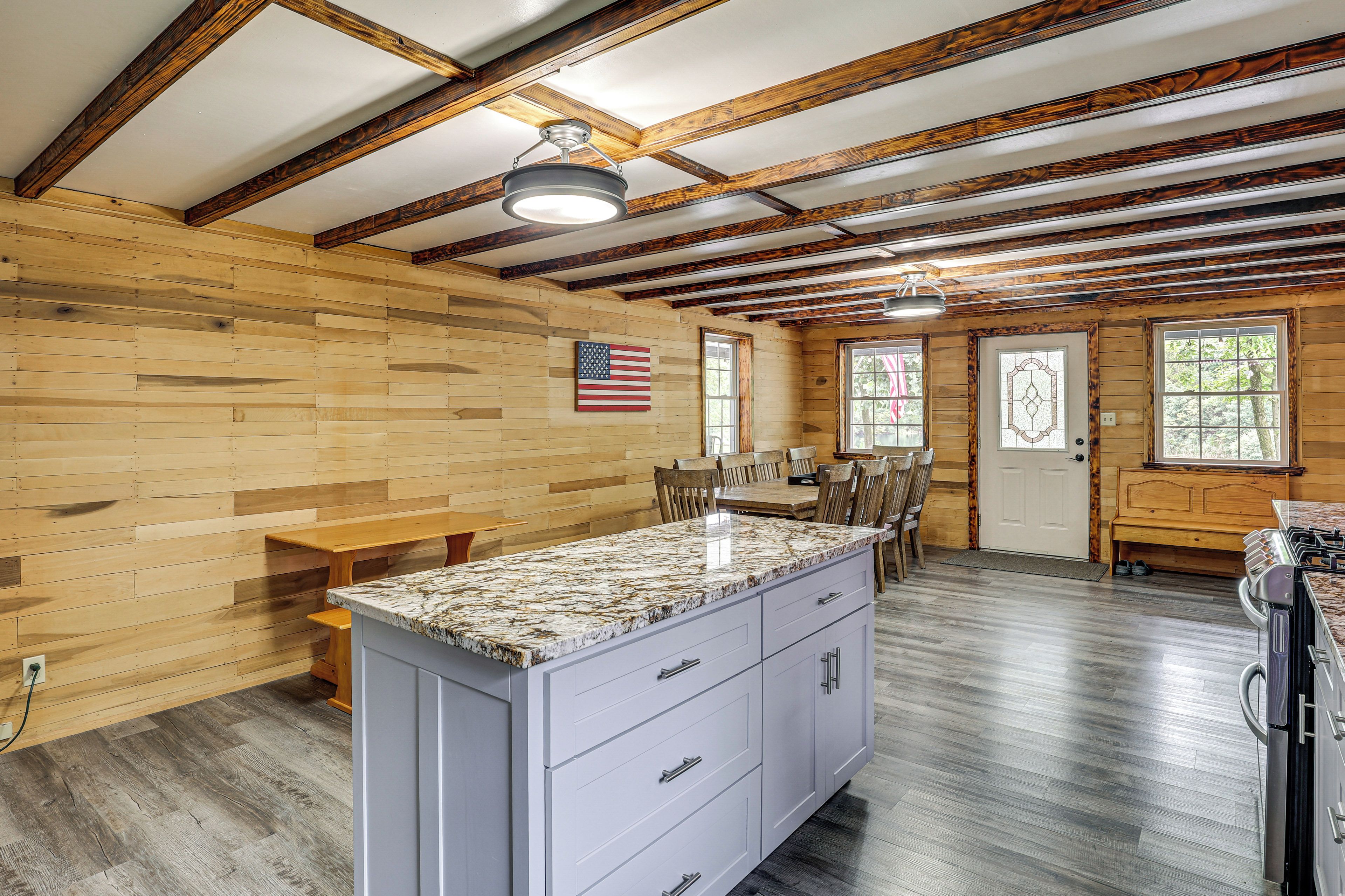 A spacious kitchen with a granite countertop, wooden beams, and a large window.
