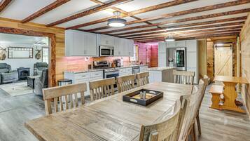 Un interior rústico con vigas de madera a la vista, un comedor con mesa y sillas de madera, y una cocina con electrodomésticos modernos.