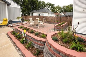 Um quintal com um alpendre, móveis de jardim e um jardim com diversas plantas.