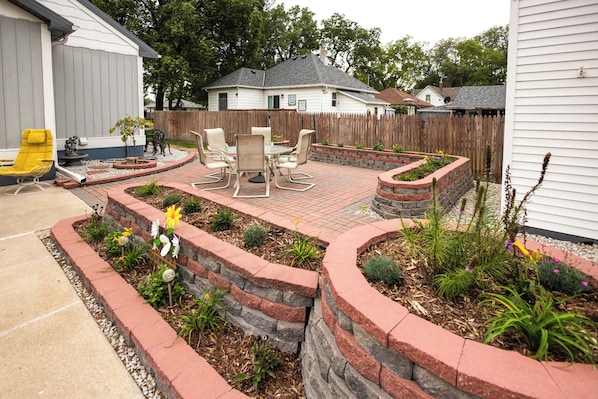 A backyard with a patio, outdoor furniture, and a garden with various plants.