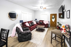 A living room with a sectional sofa, a loveseat, a coffee table, and a dining area with a chair and table. - The Play House: Family Retreat 2 Mi to Pawnee Park (Columbus)