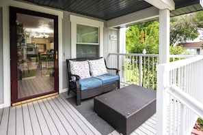 A covered porch with a wicker sofa, a small table, and a view of the backyard. - The Play House: Family Retreat 2 Mi to Pawnee Park (Columbus)