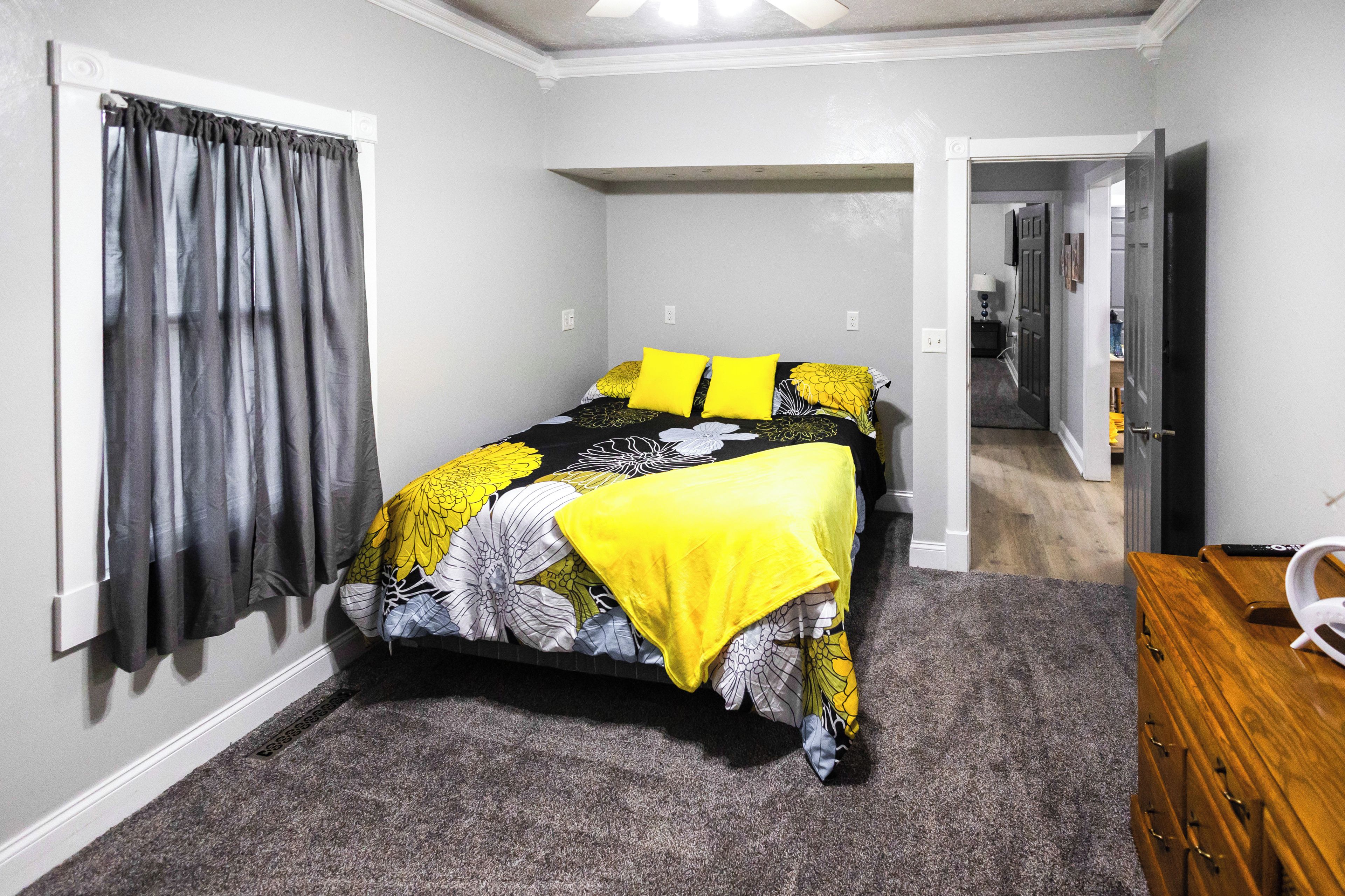 Une chambre à coucher avec un lit, une fenêtre avec des rideaux, une porte et une commode en bois.