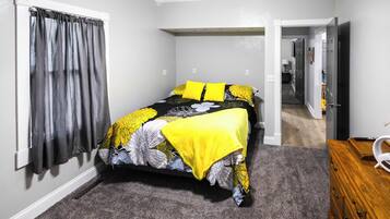 Une chambre à coucher avec un lit, une fenêtre avec des rideaux, une porte et une commode en bois.
