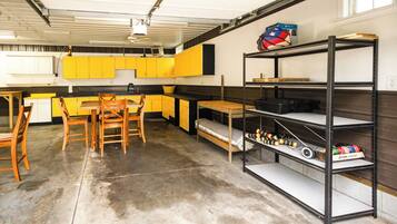 A garage with a kitchen area, wooden chairs, a table, and shelves with various items.