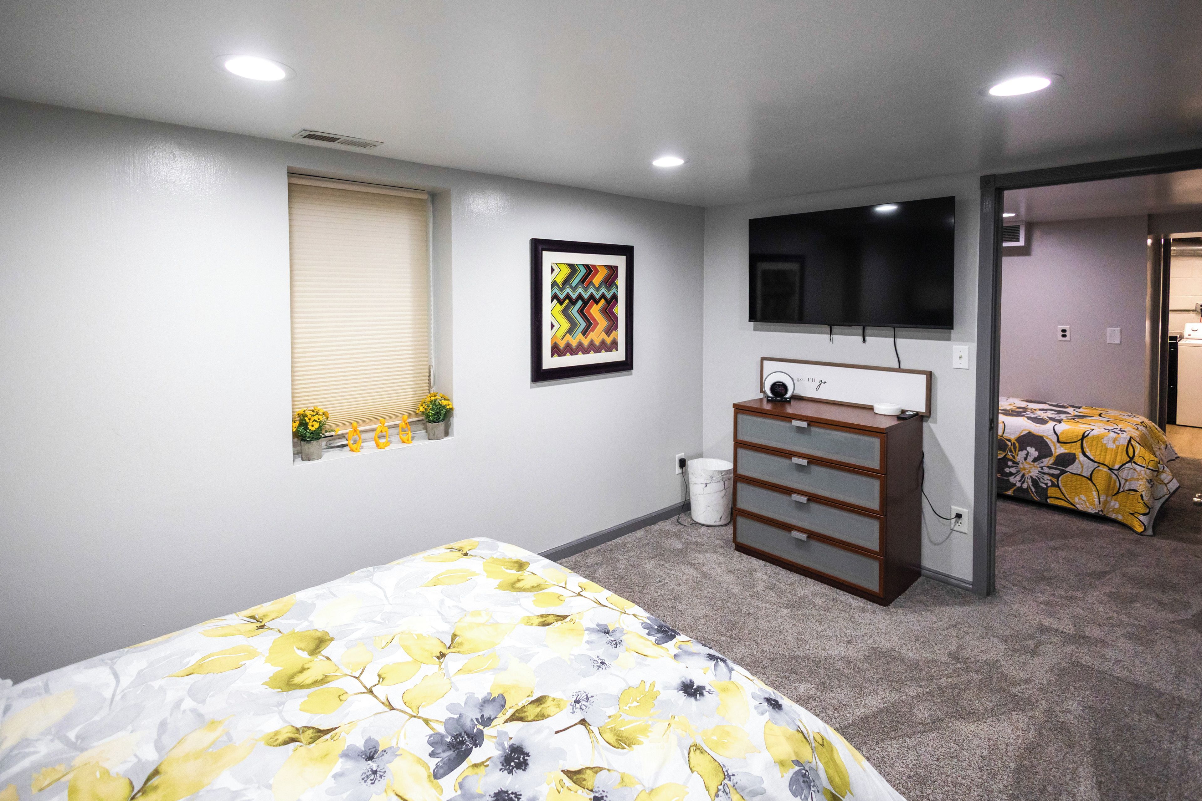 A bedroom with two beds, a dresser, a television, and a window with blinds.