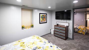 A bedroom with two beds, a dresser, a television, and a window with blinds.