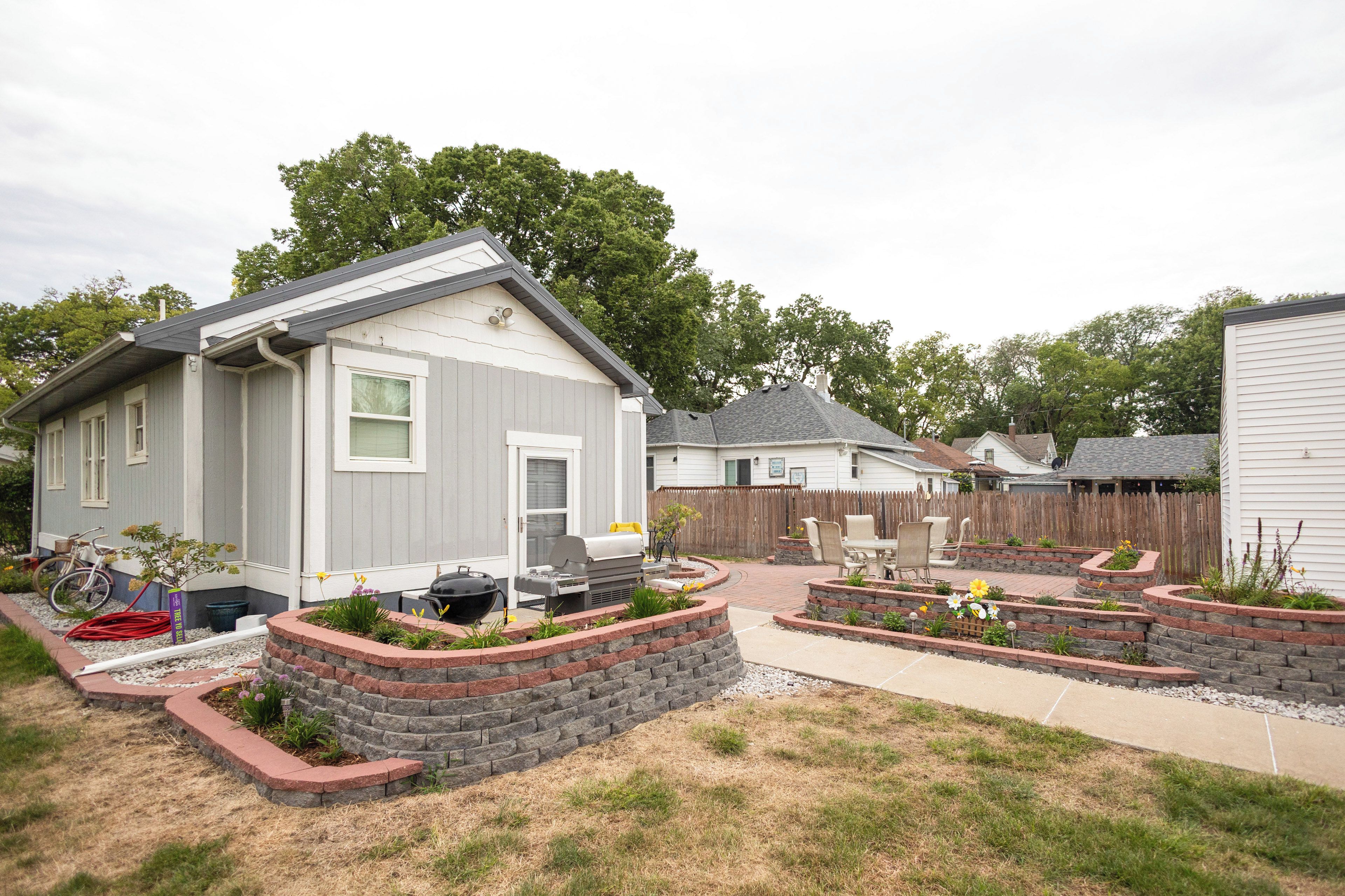 Un quartier résidentiel avec des maisons, un barbecue et un jardin agrémenté de parterres surélevés.