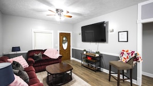 A living room with a dark red sofa, a wooden coffee table, a television mounted on the wall, and a door with a glass panel. - The Play House: Family Retreat 2 Mi to Pawnee Park (Columbus)