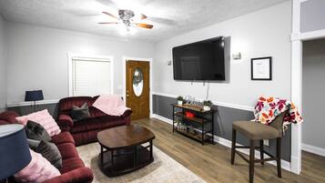 A living room with a dark red sofa, a wooden coffee table, a television mounted on the wall, and a door with a glass panel.