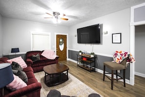 A living room with a dark red sofa, a wooden coffee table, a television mounted on the wall, and a door with a glass panel. - The Play House: Family Retreat 2 Mi to Pawnee Park (Columbus)