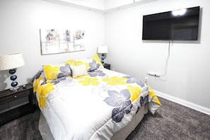 Un dormitorio con cama, televisión montada en la pared y mesita de noche con lámpara.
