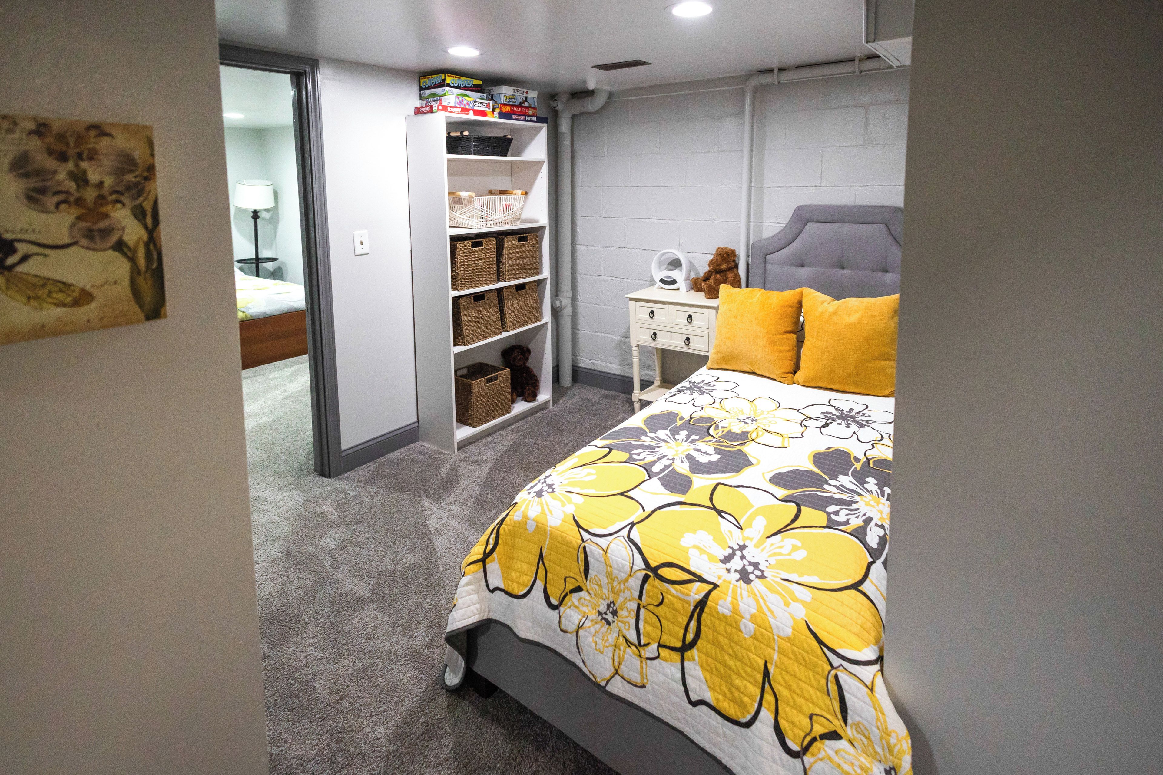 A bedroom with a bed, a nightstand, a teddy bear, and a shelf with storage baskets.