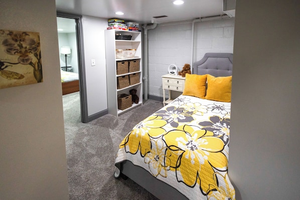 A bedroom with a bed, a nightstand, a teddy bear, and a shelf with storage baskets.
