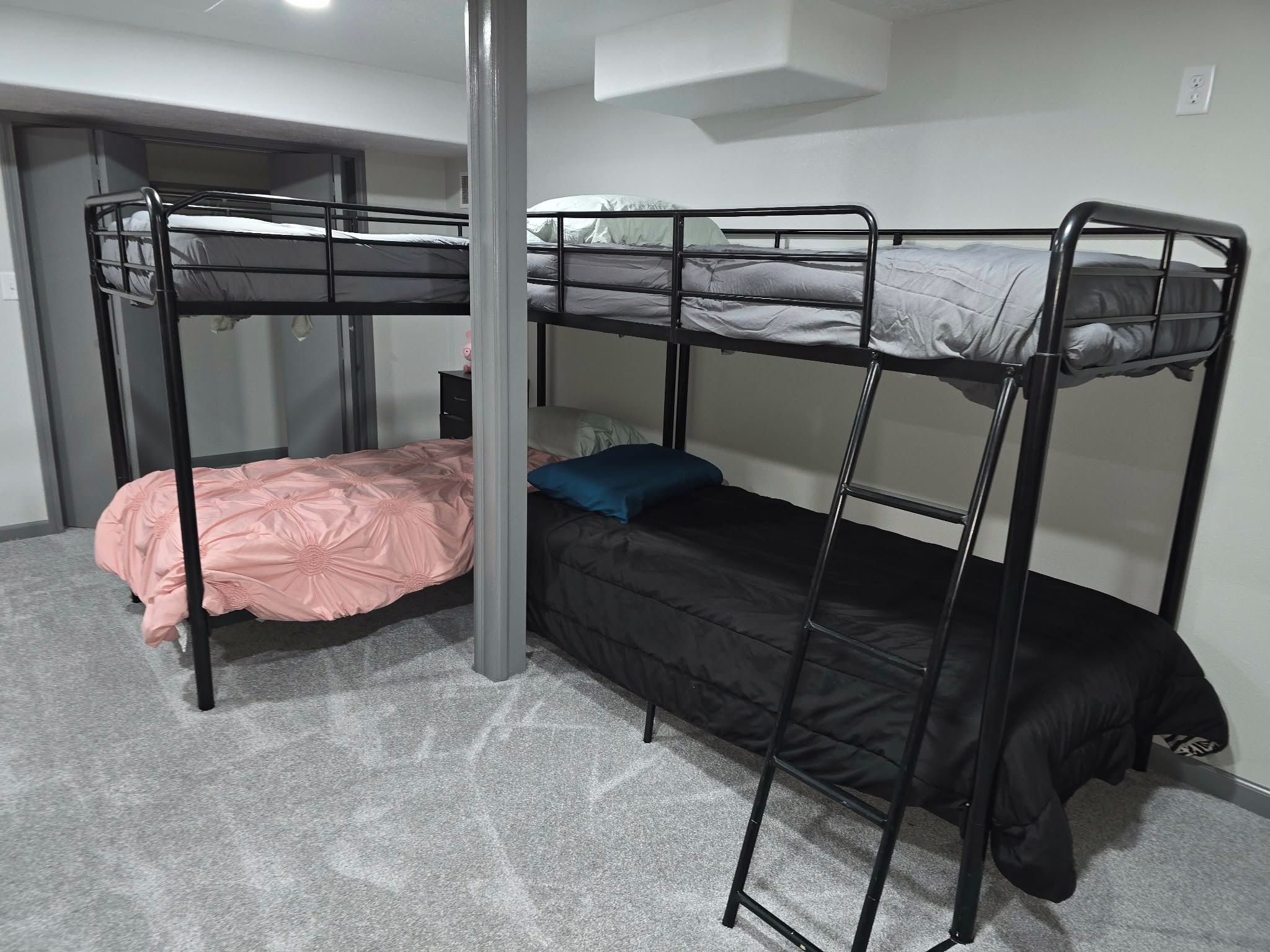 A bunk bed room with a grey carpet, a white wall, and a door in the background.