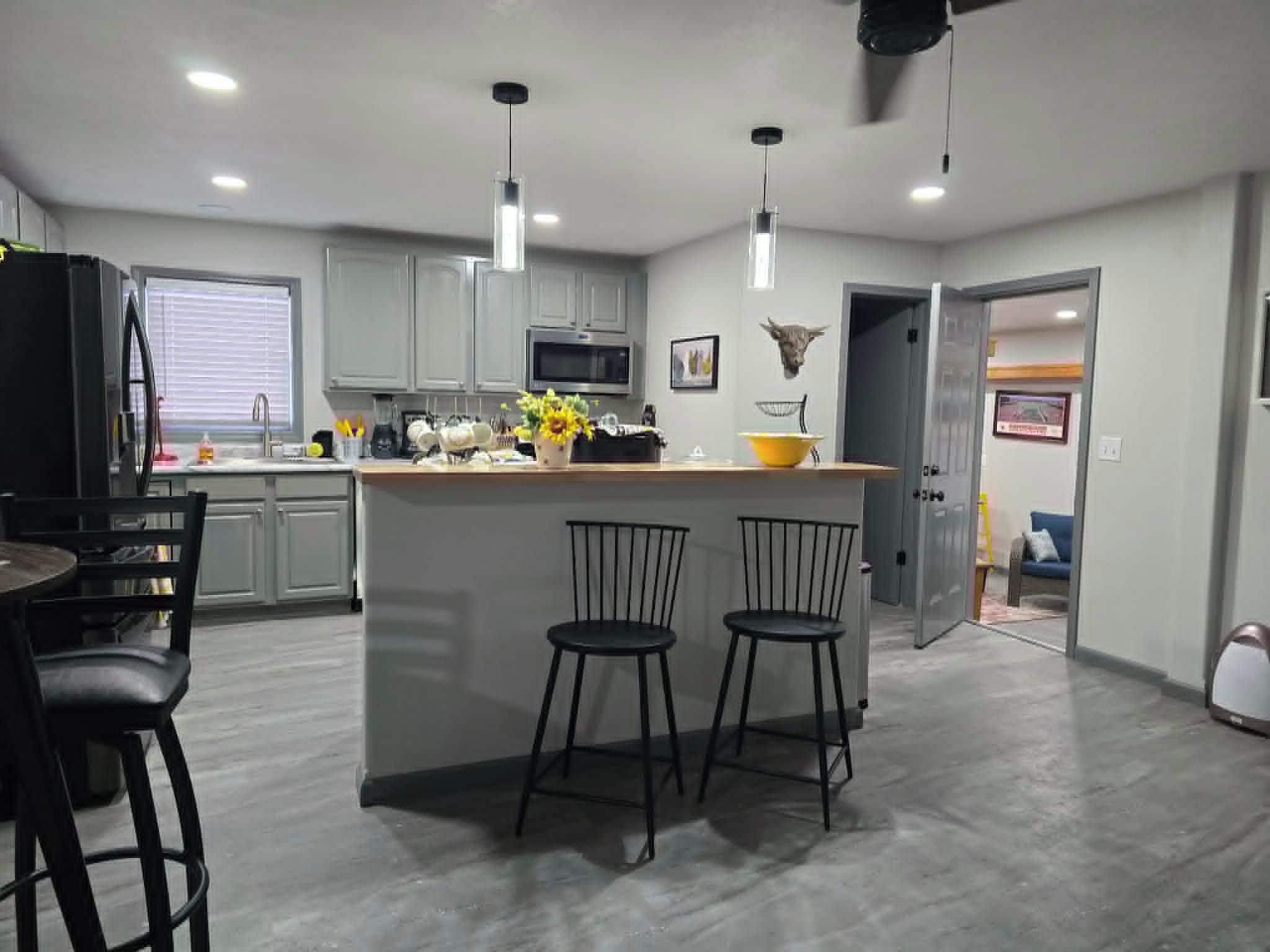 A modern kitchen with a central island, bar stools, and a dining area with a table and chairs.