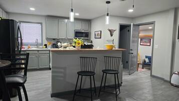 A modern kitchen with a central island, bar stools, and a dining area with a table and chairs.