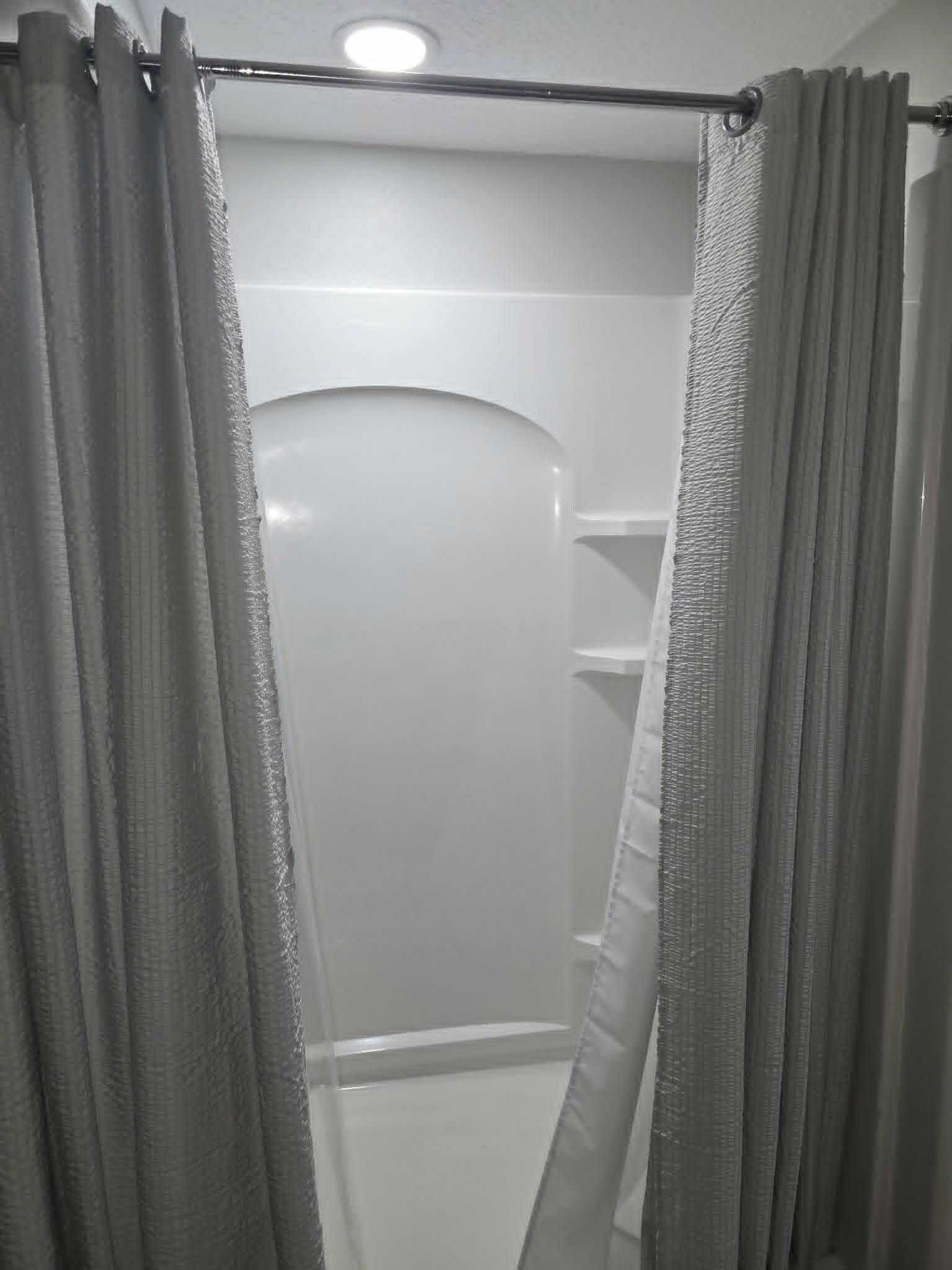 A shower area with a glass door and a metal curtain rod.