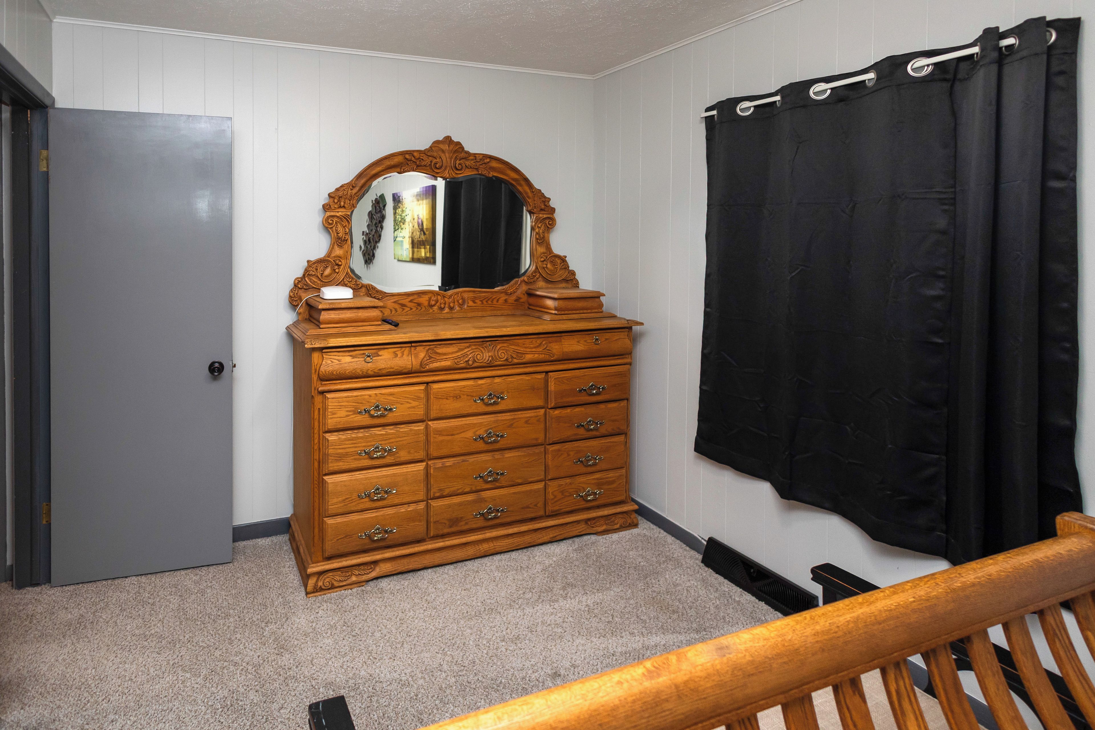 Quarto com cômoda de madeira, espelho, cortina preta e uma porta.