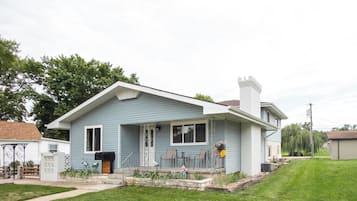 A single-story house with a front porch, a chimney, and a small garden area.