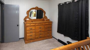 A bedroom with a wooden dresser, a mirror, a black curtain, and a door.
