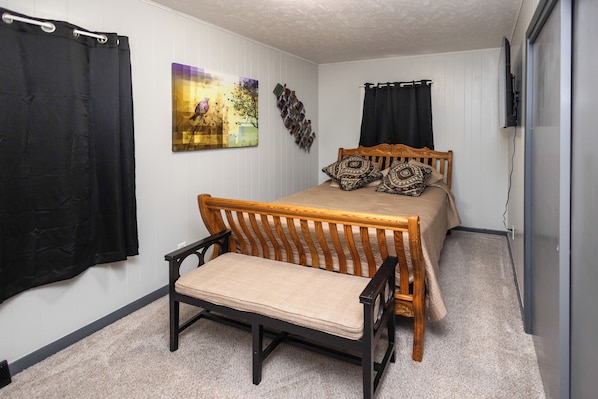 A bedroom with a bed, a chair, a wall-mounted TV, and a painting.