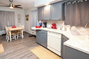 Una cocina compacta con armarios grises, lavavajillas y un comedor con mesa y sillas.