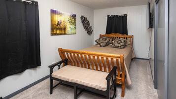 A bedroom with a bed, a chair, a wall-mounted TV, and a painting.