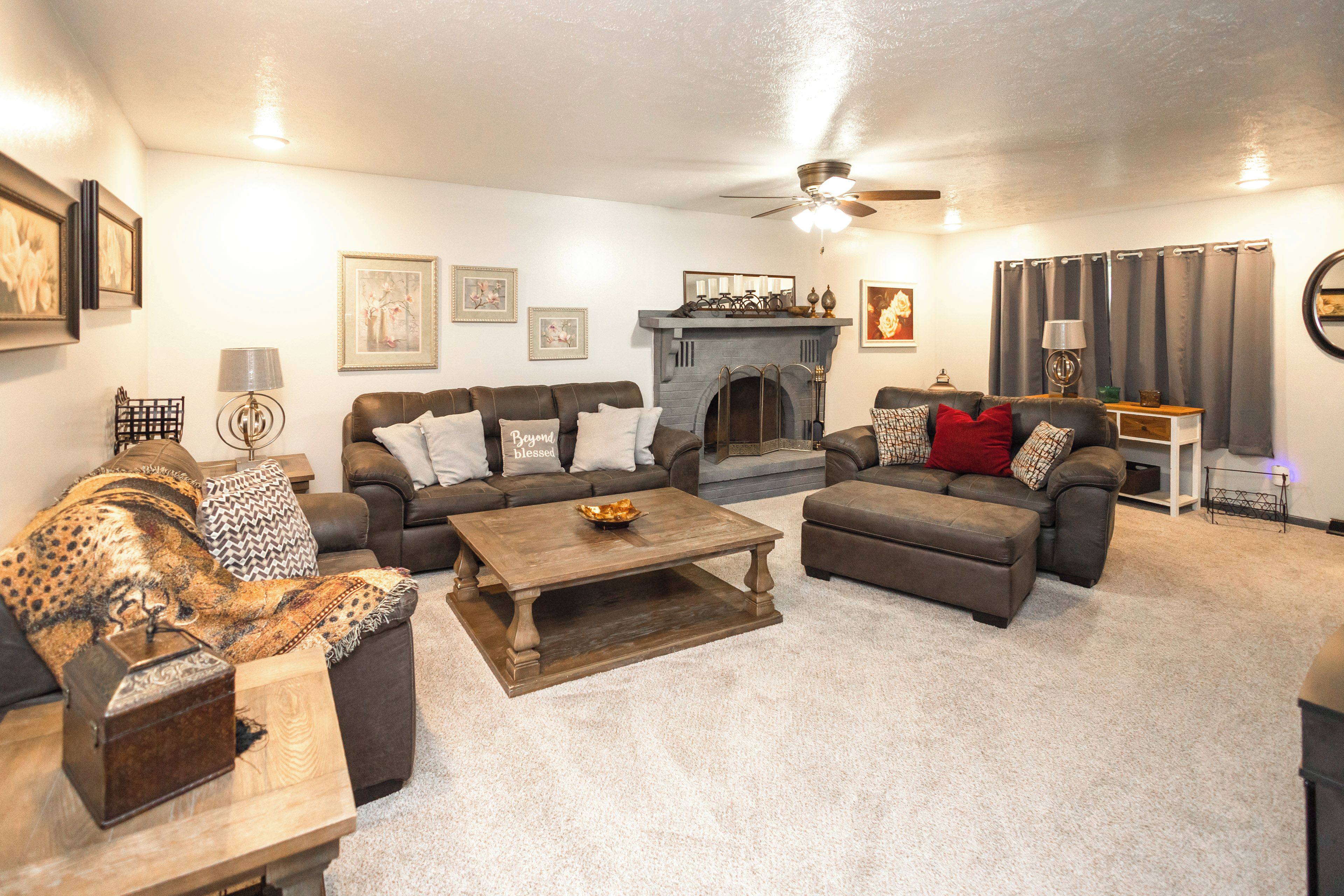A living room with a fireplace, multiple sofas, a coffee table, and a ceiling fan.