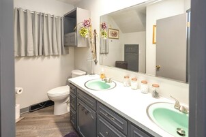 Un baño con inodoro, dos lavamanos, espejo y cortina de ducha.