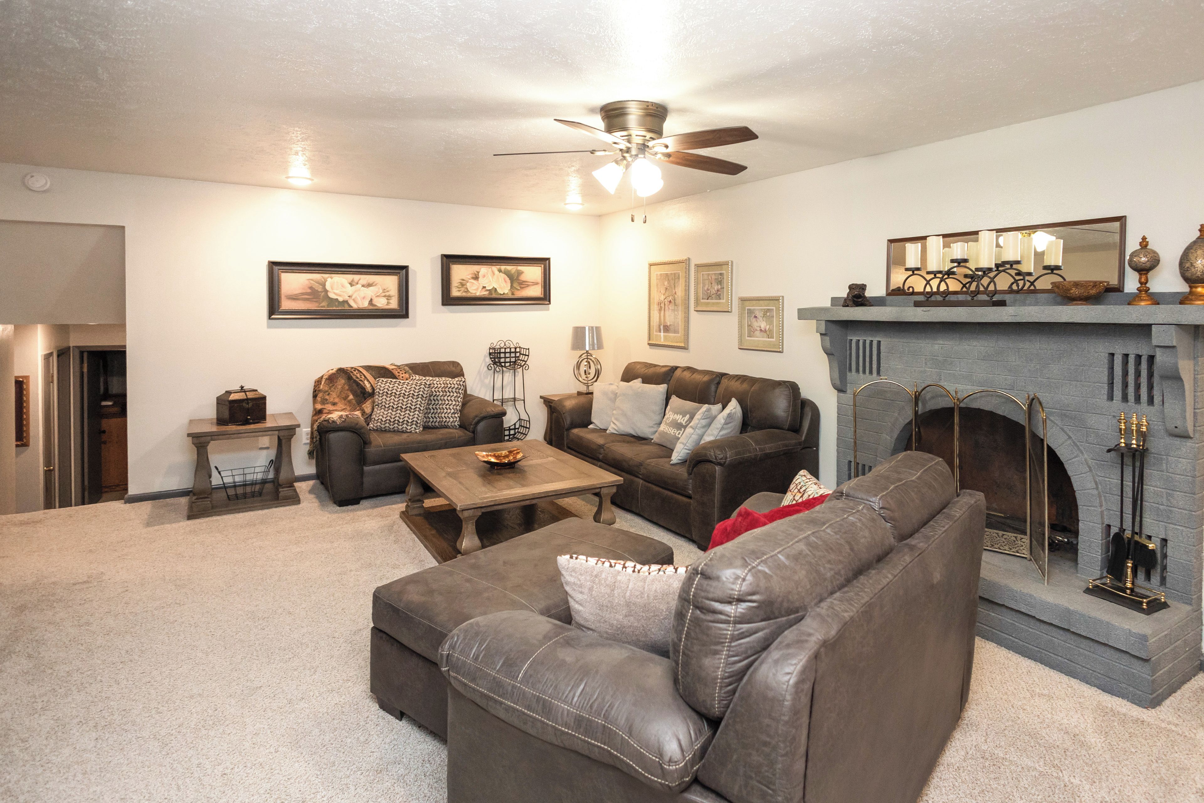 A living room with a fireplace, leather sofas, a coffee table, and a ceiling fan.
