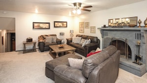 A living room with a fireplace, leather sofas, a coffee table, and a ceiling fan. - 'the Cech Inn' in Columbus: Walk to Pawnee Park! (Columbus)