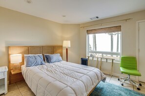 Un dormitorio con cama, mesita de noche, lámpara, ventana con persianas y una silla.