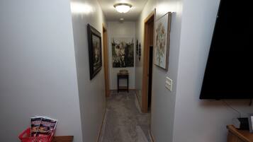 A narrow hallway with a carpeted floor, framed artwork on the walls, and a door at the end.
