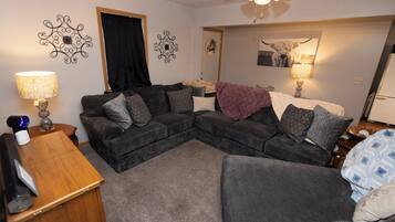 A living room with a sectional sofa, a wooden side table, a lamp, and a ceiling fan.