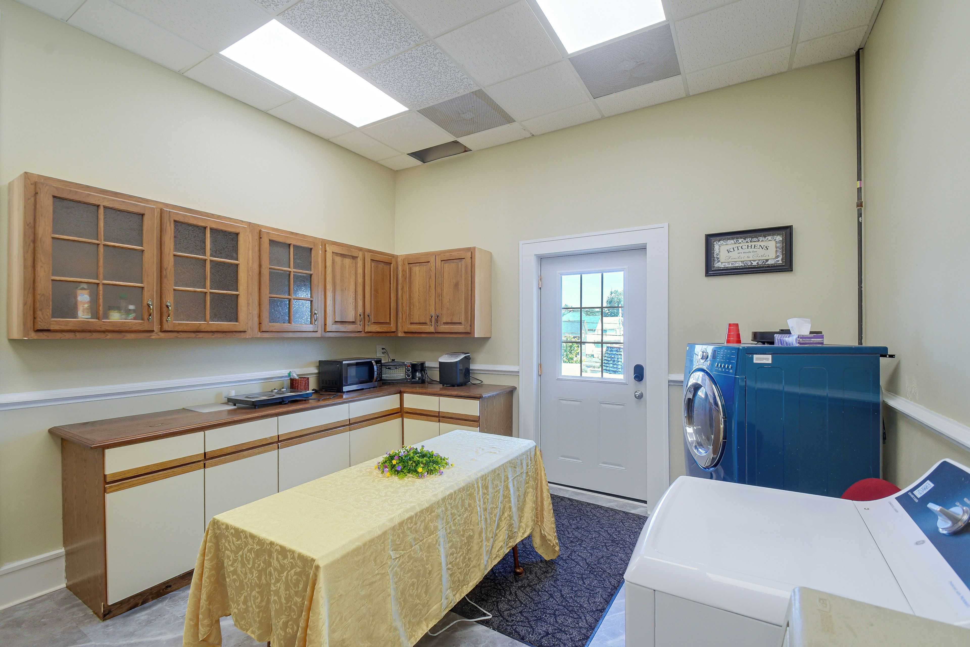 A compact kitchen with wooden cabinets, a microwave, a coffee maker, and a washing machine.