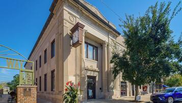 A classical building with a clock, a bench, and a tree in front.