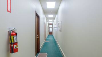 A hallway with a fire extinguisher mounted on the wall, a fire exit sign, and a door at the end.