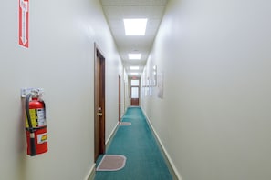 A hallway with a fire extinguisher mounted on the wall, a fire exit sign, and a door at the end.