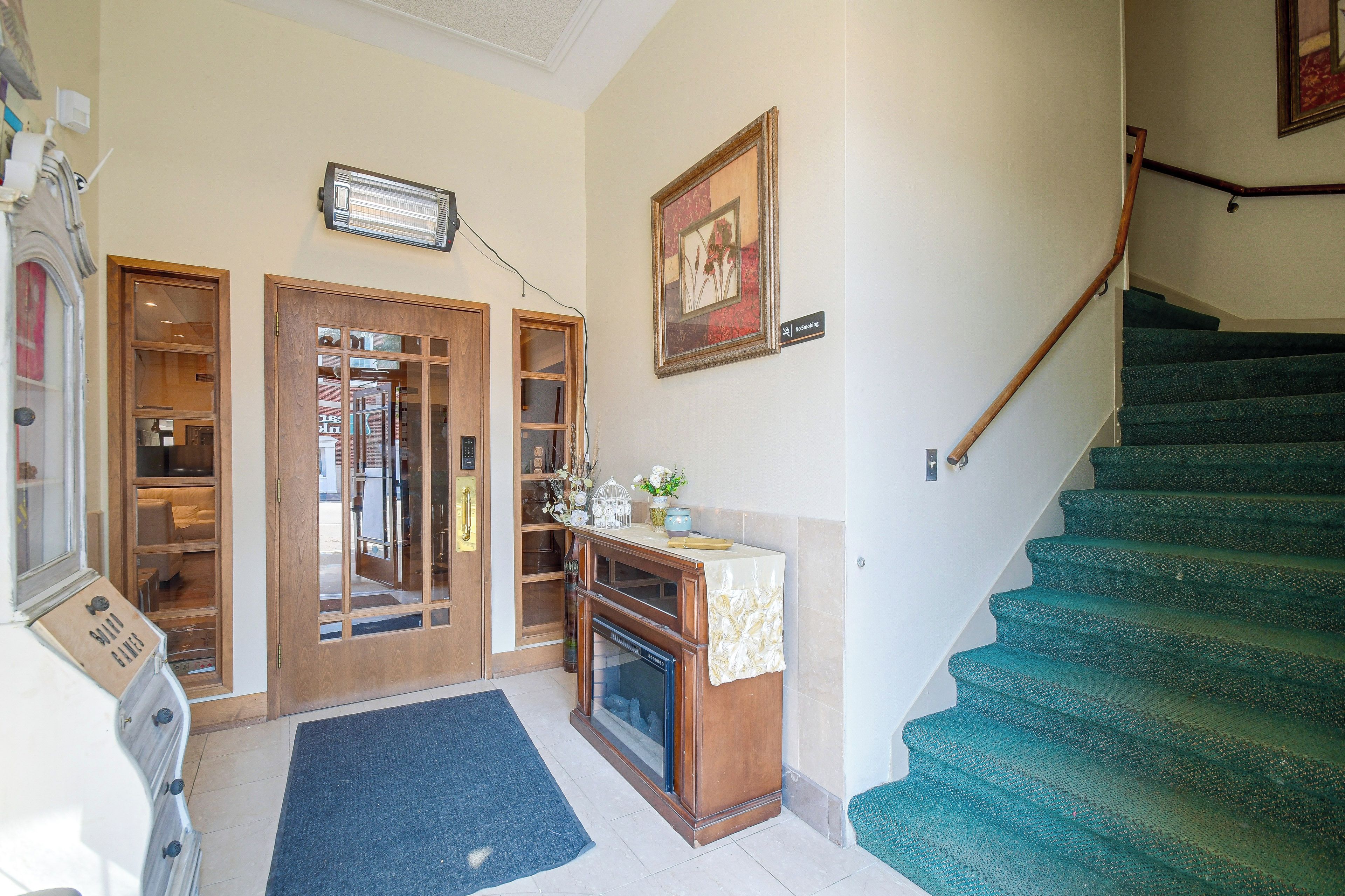 A staircase with a green carpet, a wooden door with glass panels, a wall-mounted heater, and a 'No Smoking' sign.