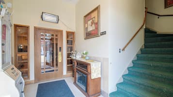 A staircase with a green carpet, a wooden door with glass panels, a wall-mounted heater, and a 'No Smoking' sign.
