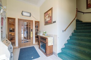 Un escalier recouvert d’une moquette verte, une porte en bois avec des panneaux de verre, un radiateur fixé au mur et un panneau indiquant « Il est interdit de fumer ».