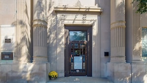 A building entrance with a dark door, flanked by two columns with decorative capitals, and a small potted plant on the ground. - Walkable Main Street Apartment in Princeton! (Princeton)