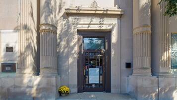 A building entrance with a dark door, flanked by two columns with decorative capitals, and a small potted plant on the ground.